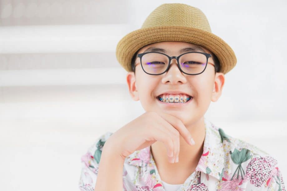 smiling teen boy with braces, black framed glasses and small straw hat