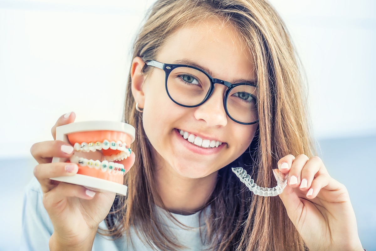 girl holding up invisalign aligner and model of teeth with braces